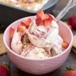 A pink bowl of strawberry cheesecake ice cream topped with diced strawberries.