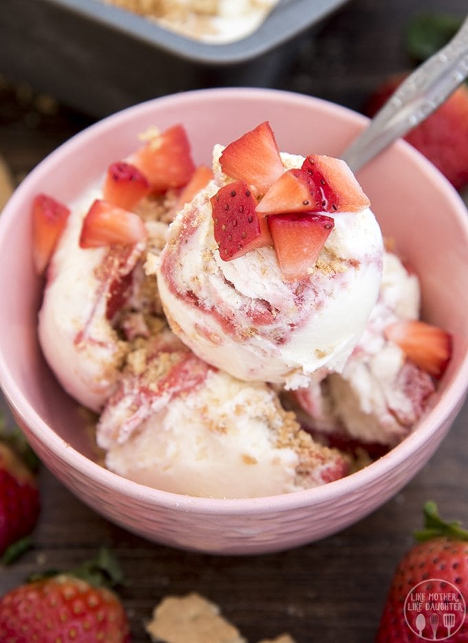 A bowl of ice cream swirled with strawberry and graham cracker crumble, topped with fresh strawberries. 