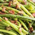 A close up of a pile of green beans topped with bacon and sauteed onions.
