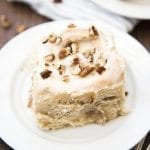 A banana cinnamon roll on a plate topped with icing and chopped pecans.
