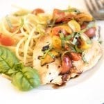 A plate of spaghetti with a grilled chicken breast topped with tomatoes, balsamic glaze, and fresh basil.