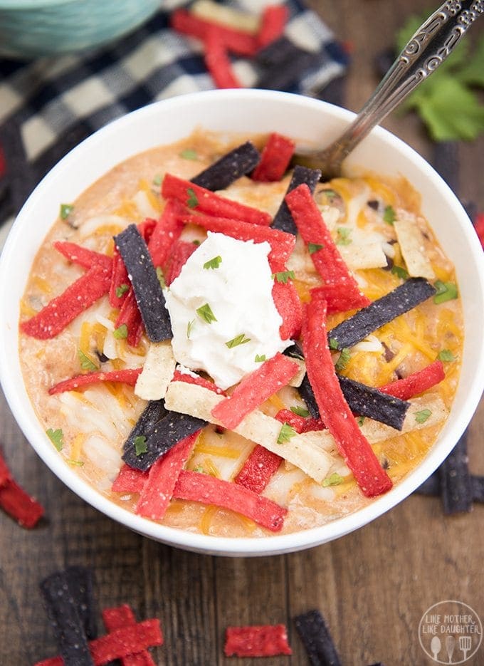 A bowl of creamy enchilada soup topped with tortilla strips and sour cream.