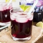Glasses of a purple grape drink topped with lime slices.