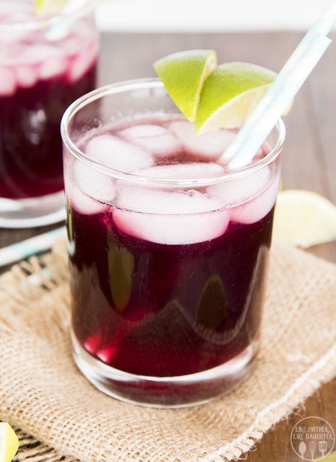 A glass of a purple grape lime rickey drink topped with lime slices.