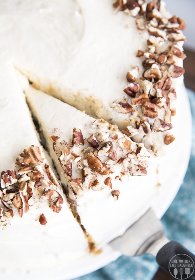 A piece of a round carrot cake with one slice cut out of it.