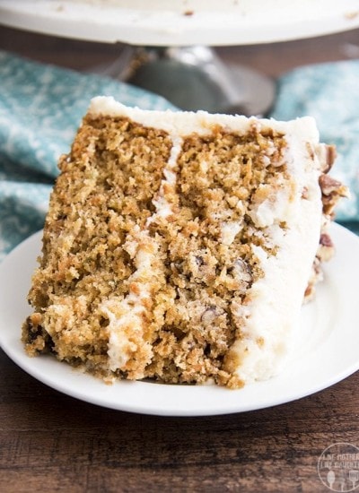 A slice of layered carrot cake is displayed on a plate with frosting.