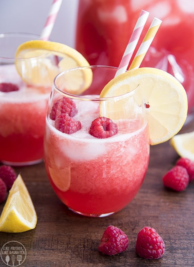 A glass of raspberry lemonade topped with fresh raspberries and a lemon slice. 