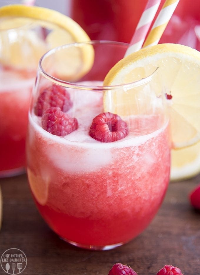 A glass of raspberry lemonade topped with raspberries and a lemon slice. 