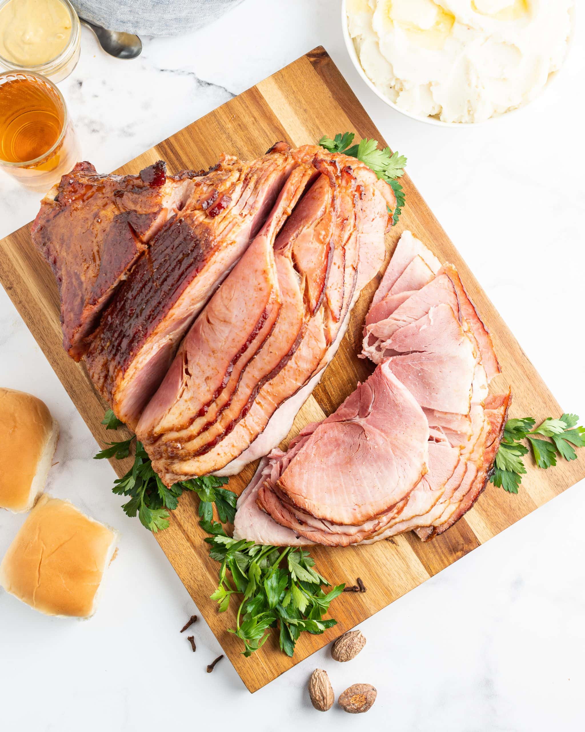 An overhead shot of a maple glazed ham on a cutting board, some of the pieces are cut off and laying in front of the ham on the board.