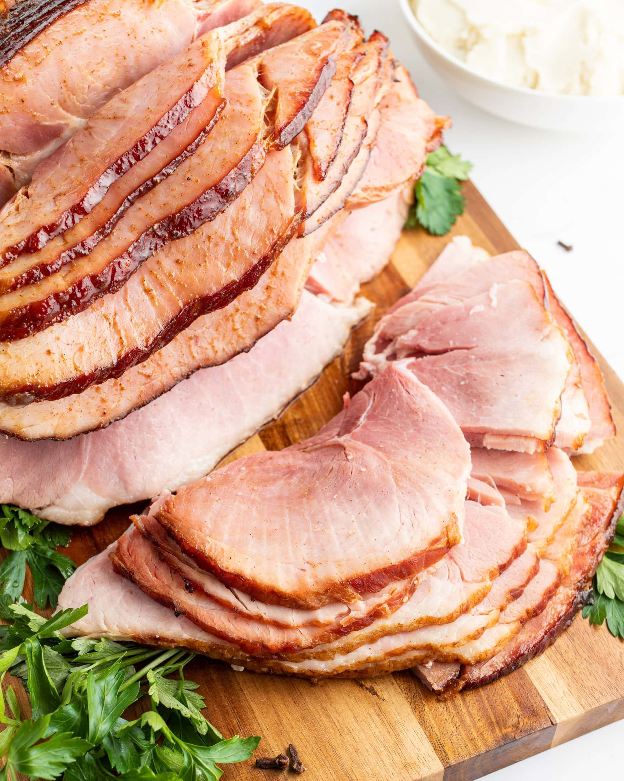 An overhead shot of a maple glazed ham on a cutting board, some of the pieces are cut off and laying in front of the ham on the board.