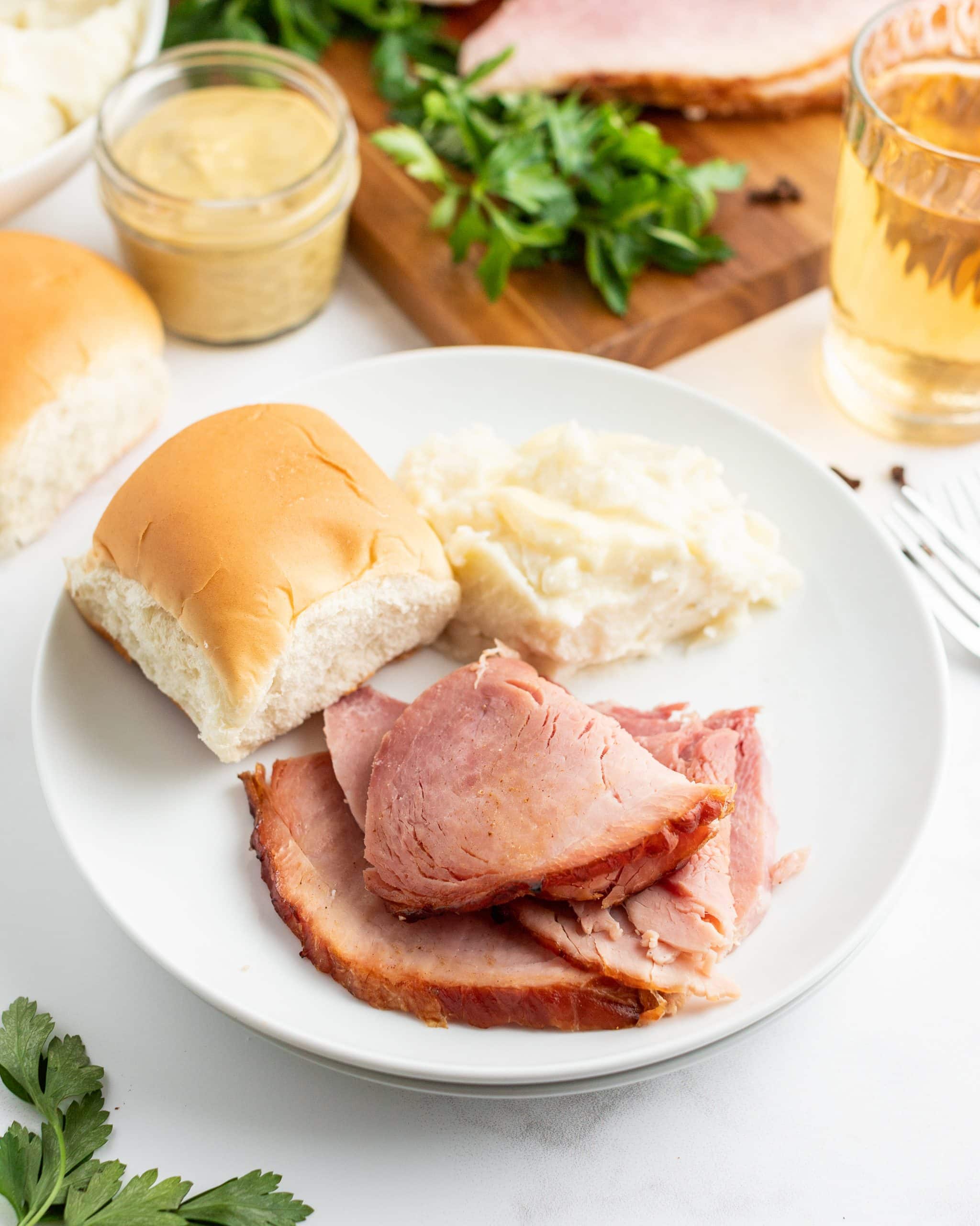 Slices of ham on a dinner plate with a roll and mashed potatoes.