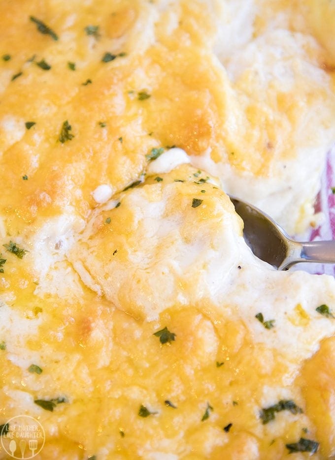 A spoon scooping into a dish of cheesy scalloped potatoes, showing the white sauce and cheese on top.