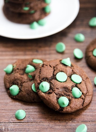 Two chocolate and mint chip cookies on a wooden table.