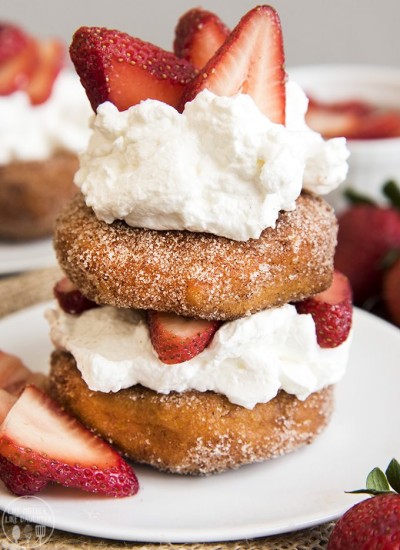 Two cinnamon sugar donuts topped with whipped cream and sliced strawberries.