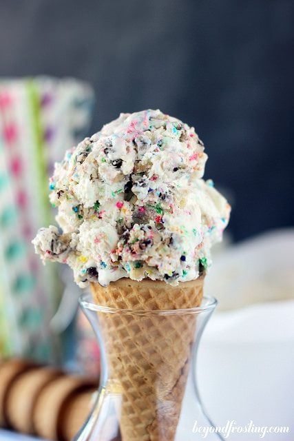 An ice cream cone filled with cake batter and cookie dough ice cream with lots of sprinkles. 