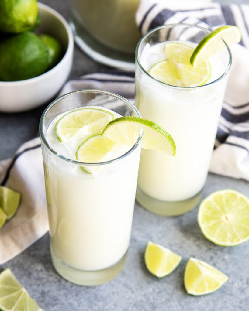 Two glasses of Brazilian limeade topped with lime slices, and ice.