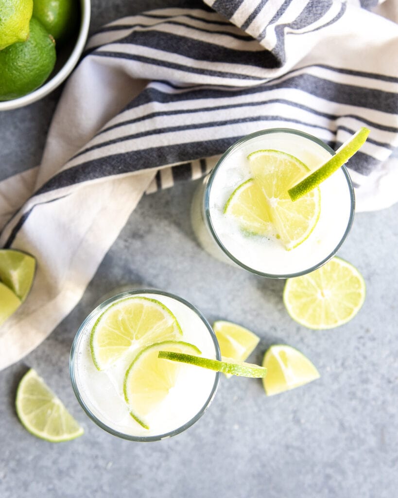 An overhead photo of two glasses of Brazilian lemonade, topped with lime slices.