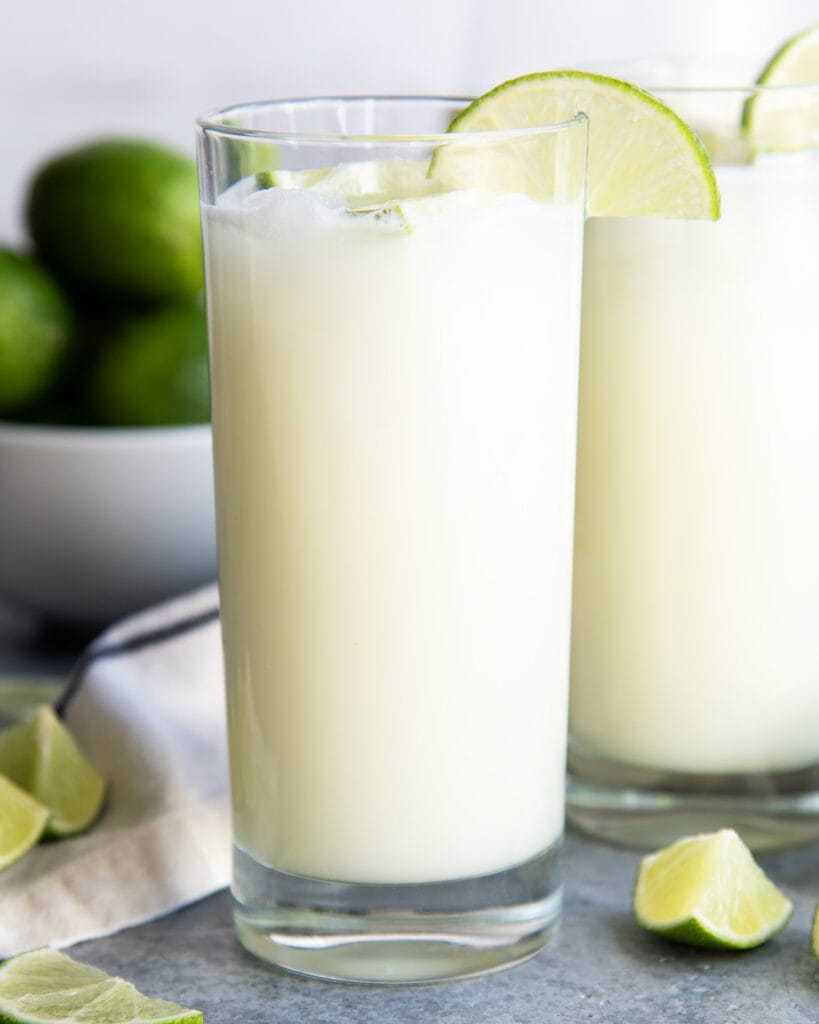 A glass of a creamy liquid that is brazilian limeade, topped with a lime slice.