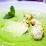 A close up of a green asaparagus soup in a bowl topped with croutons and parmesan cheese.