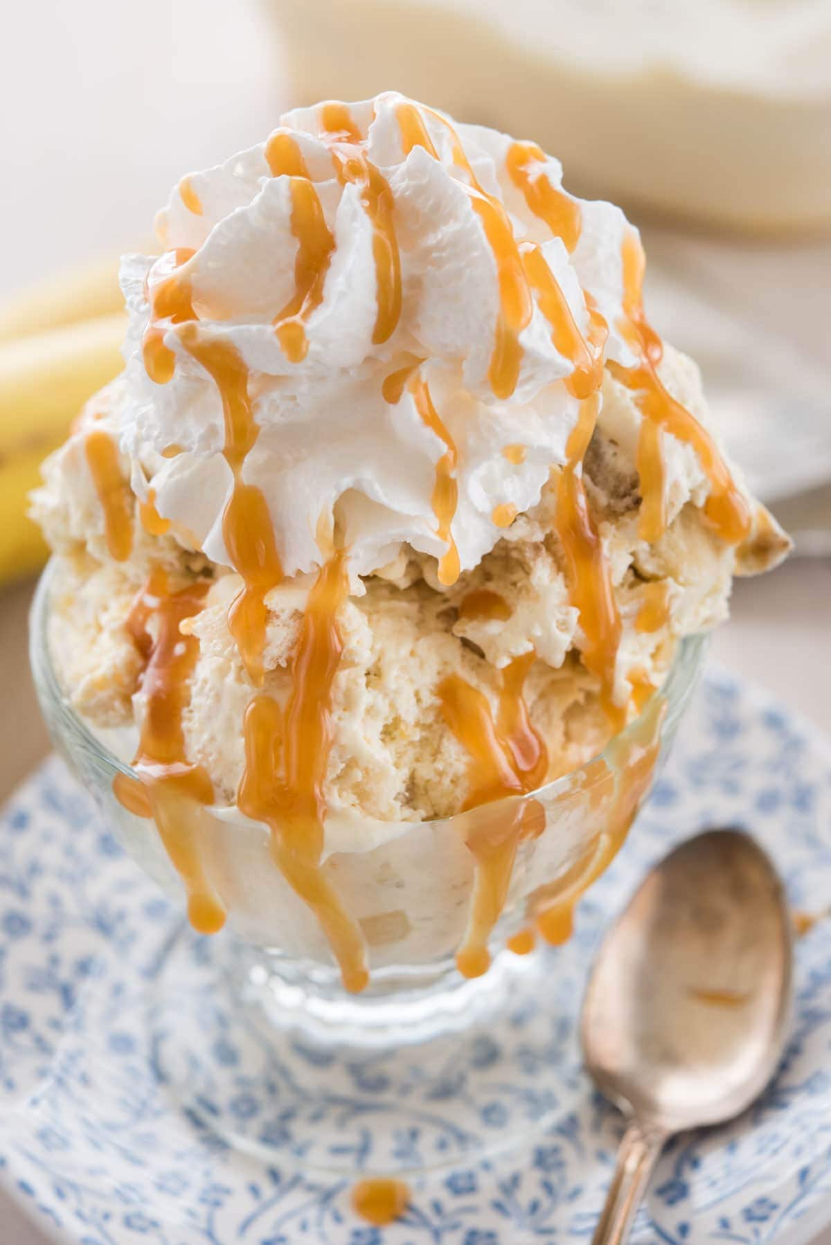 A glass bowl of banana cream pie ice cream topped with whipped cream and caramel syrup. 