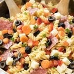 A close up of a bowl of pasta salad with salami, carrots, olives, and pasta.