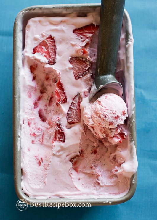An overhead photo of a container of strawberry ice cream with fresh strawberry slices in it. 