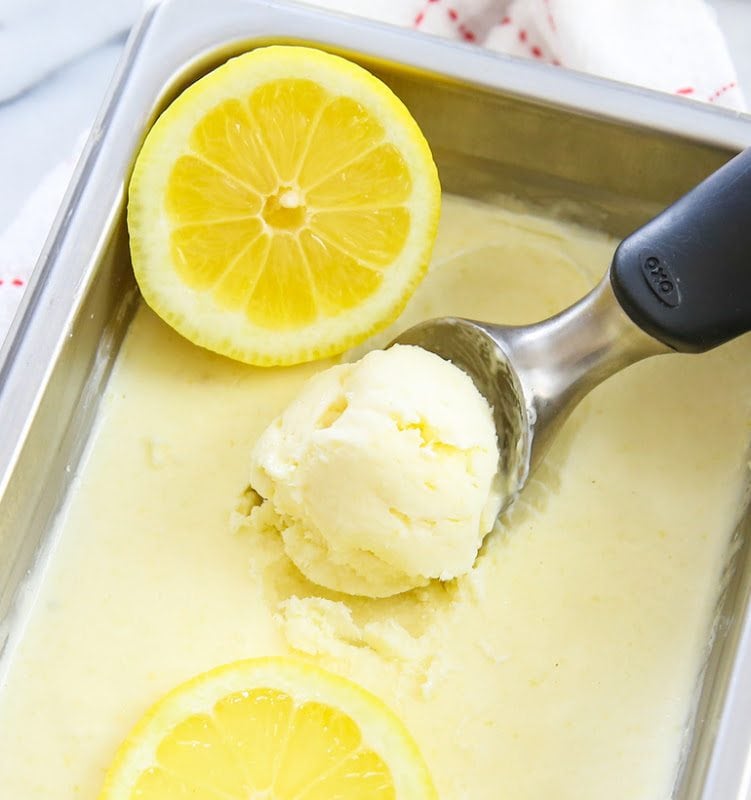 A container of lemon ice cream with an ice cream scoop in it. 