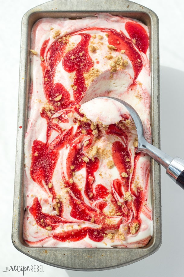 A bread pan full of cherry cheesecake ice cream with an ice cream scoop, scooping into it. 