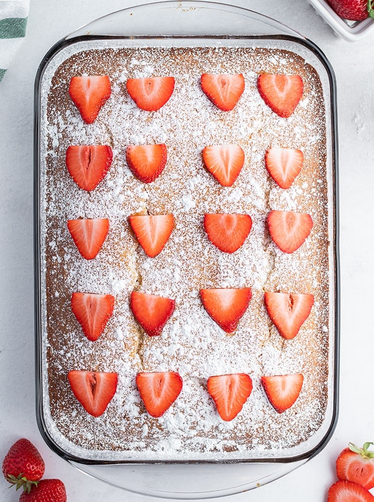 A strawberry yogurt cake topped with powdered sugar and sliced strawberries