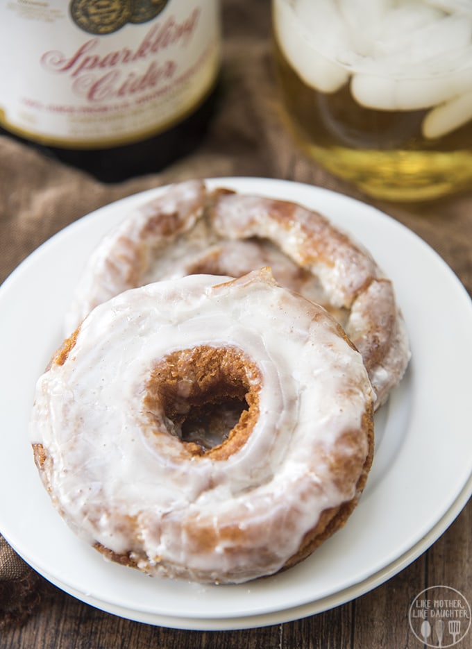 Two apple cider donuts on a plate topped with a white glaze. 