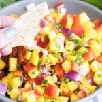 A hand holding a chip dipped into fresh mango salsa.