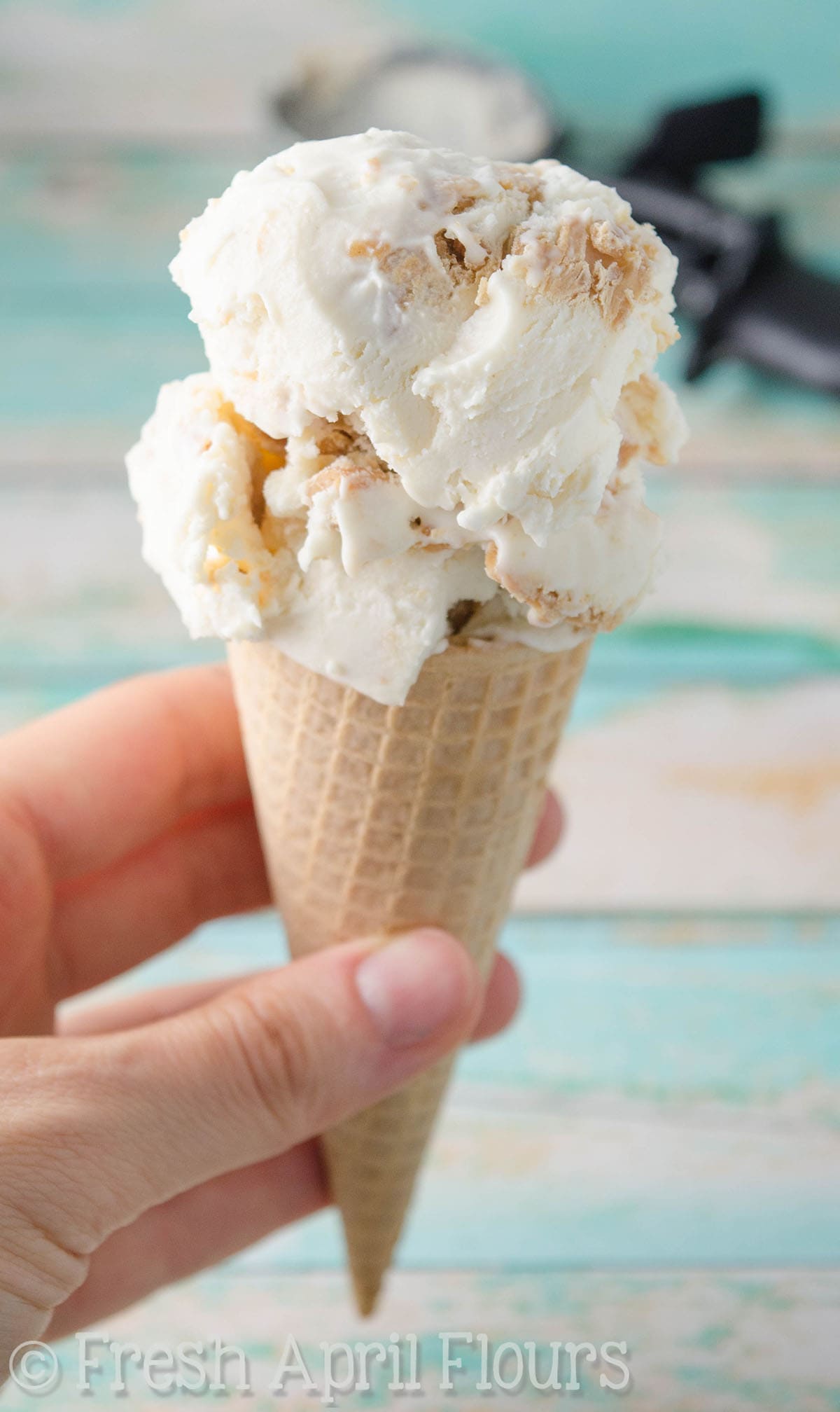 A hand holding an ice cream cone with two scoops of peanut butter ripple ice cream on top. 