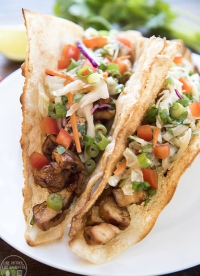 Two teriyaki chicken wonto tacos topped with green onion, bell pepper, and carrots.