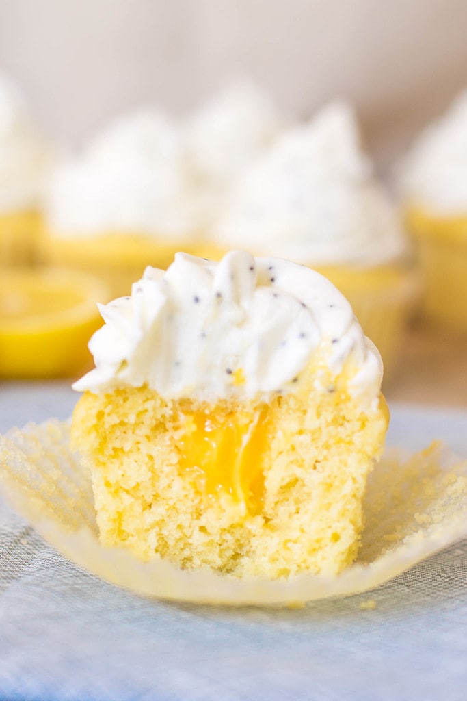 A cut open lemon cupcake filled with lemon curd and topped with a white frosting full of poppyseeds. 