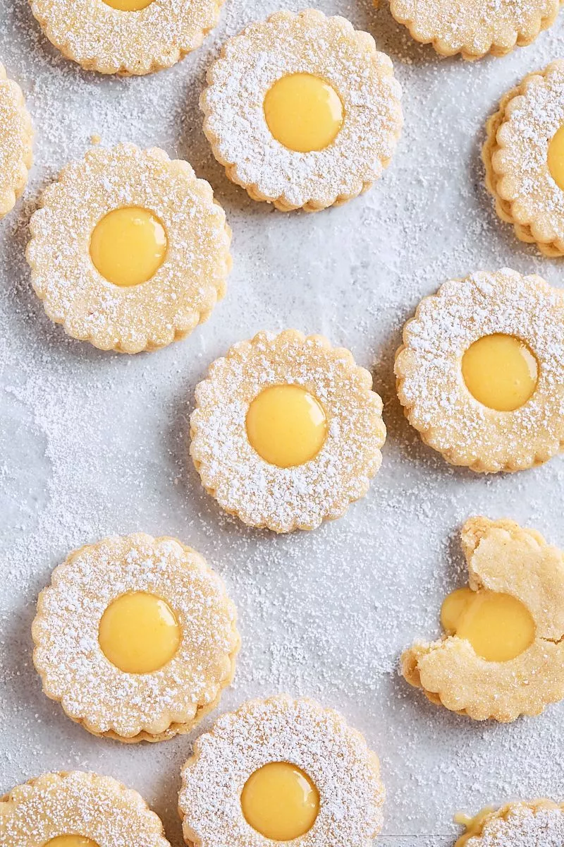 An overhead photo of lemon curd filled linzer cookie sandwiches on a piece of parchment paper.