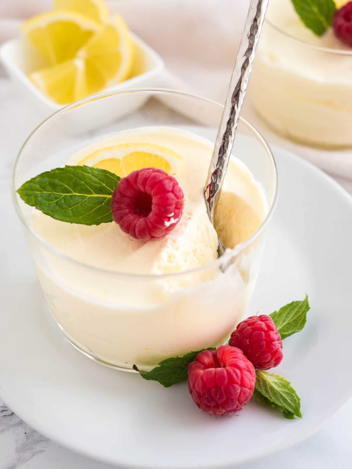Lemon curd mousse in a clear glass topped with a raspberry and mint leaves. 