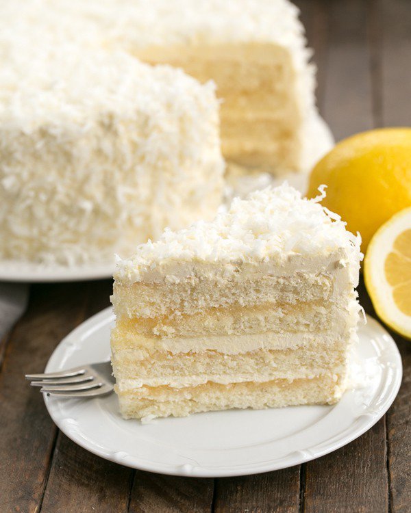 A slice of a lemon layer cake topped with a white frosting and shredded coconut on a plate. 