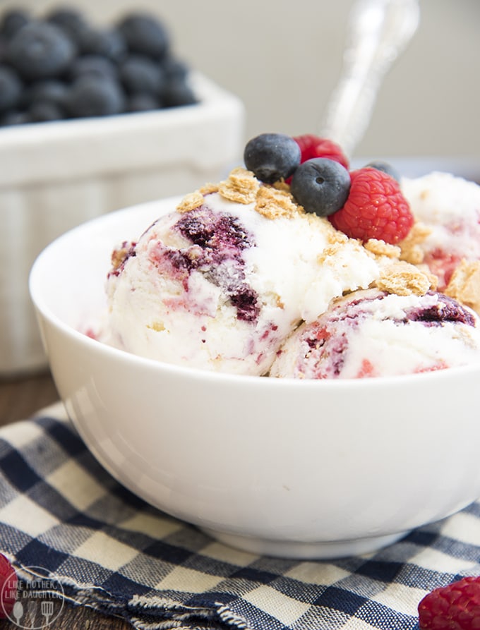 A close up of a bowl of berry swirled ice cream topped with fresh blueberries and raspberries. 