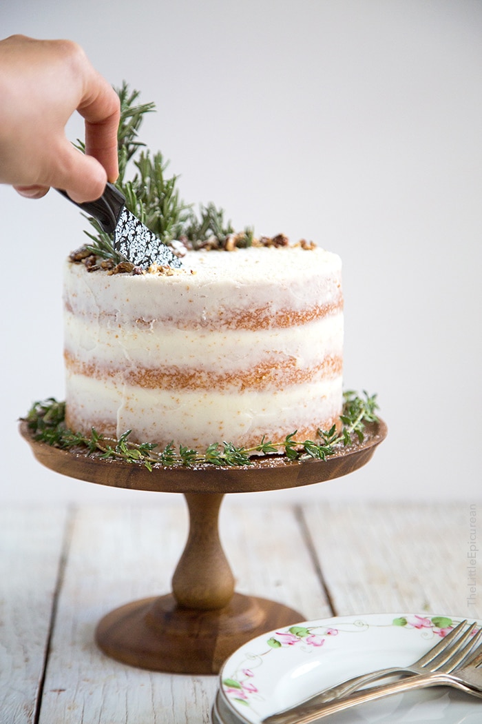 A person cutting into a naked frosted lemon and rosemary cake. 