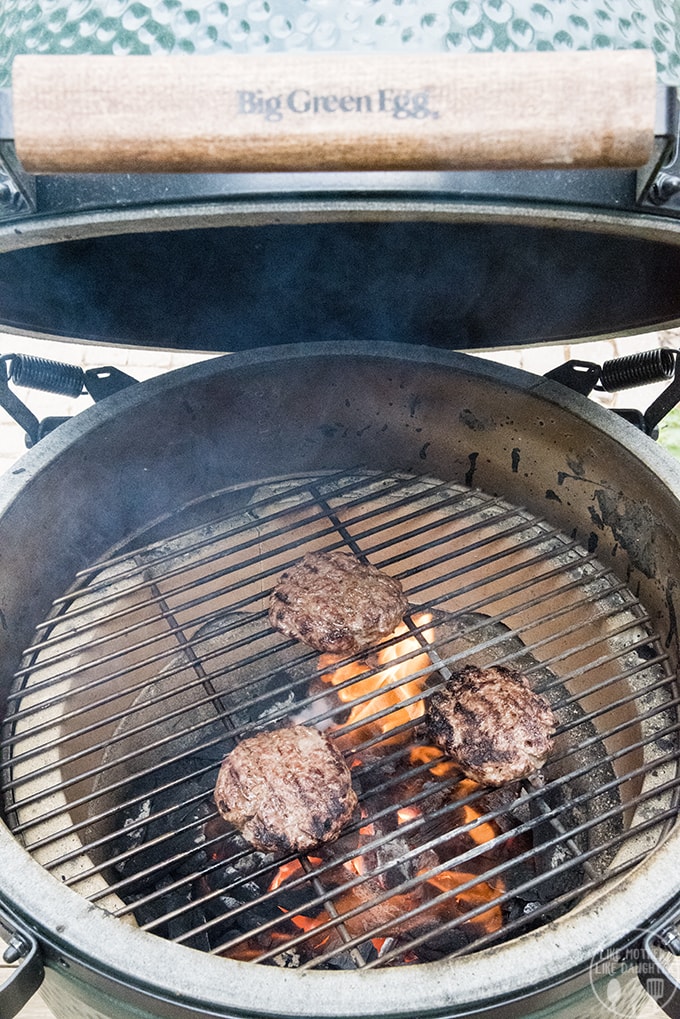 Three lamb burgers cooking on a round grill. 