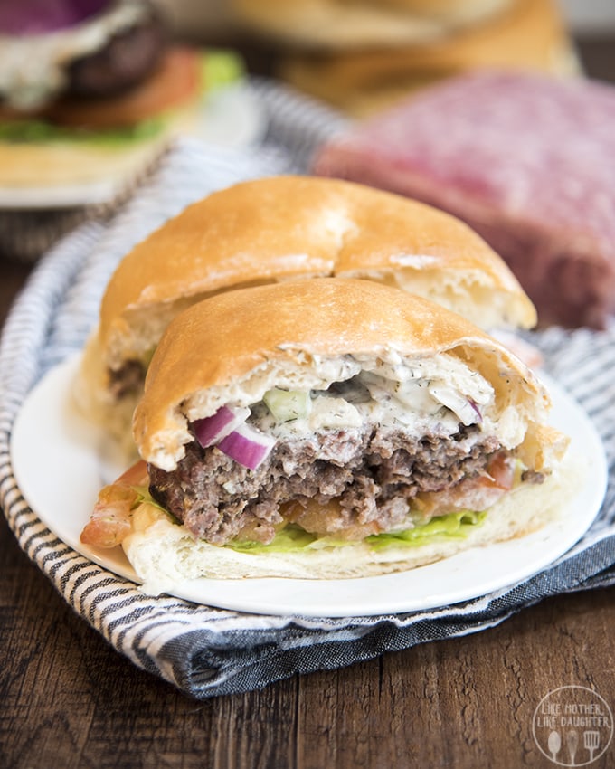 A burger cut in half on a plate. The burger is topped with red onion and a white tzatziki sauce.