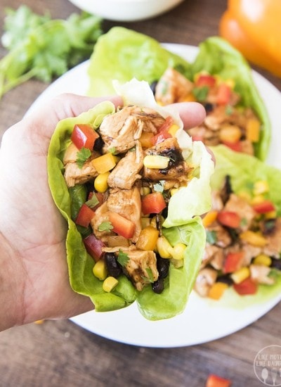A hand holding a lettuce wrap full of bbq chicken, corn, and black beans.