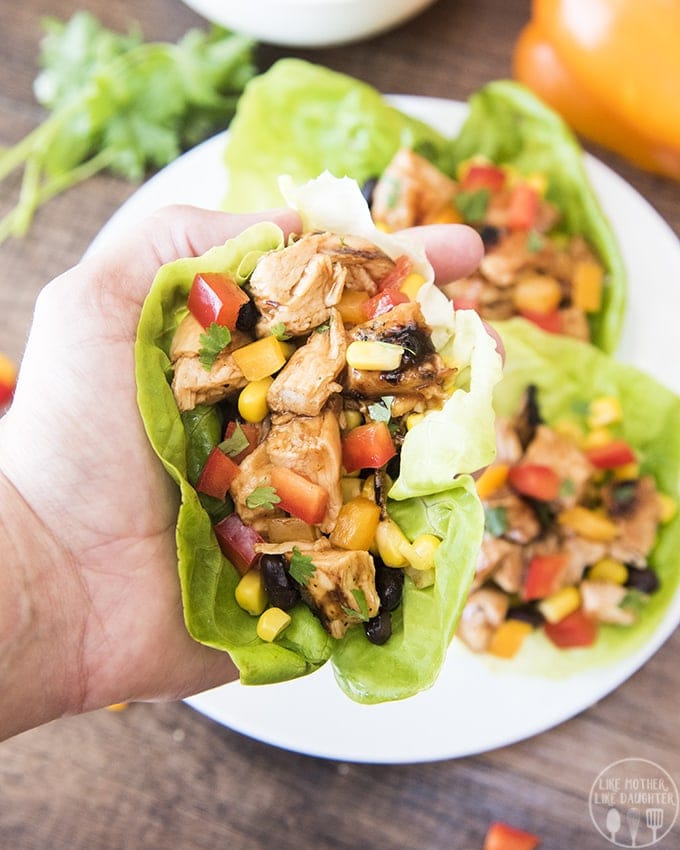 A hand holding a lettuce wrap full of bbq chicken, corn, and black beans.