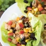 Lettuce wraps topped with bbq grilled chicken, red bell pepper, black beans, and corn on a plate.