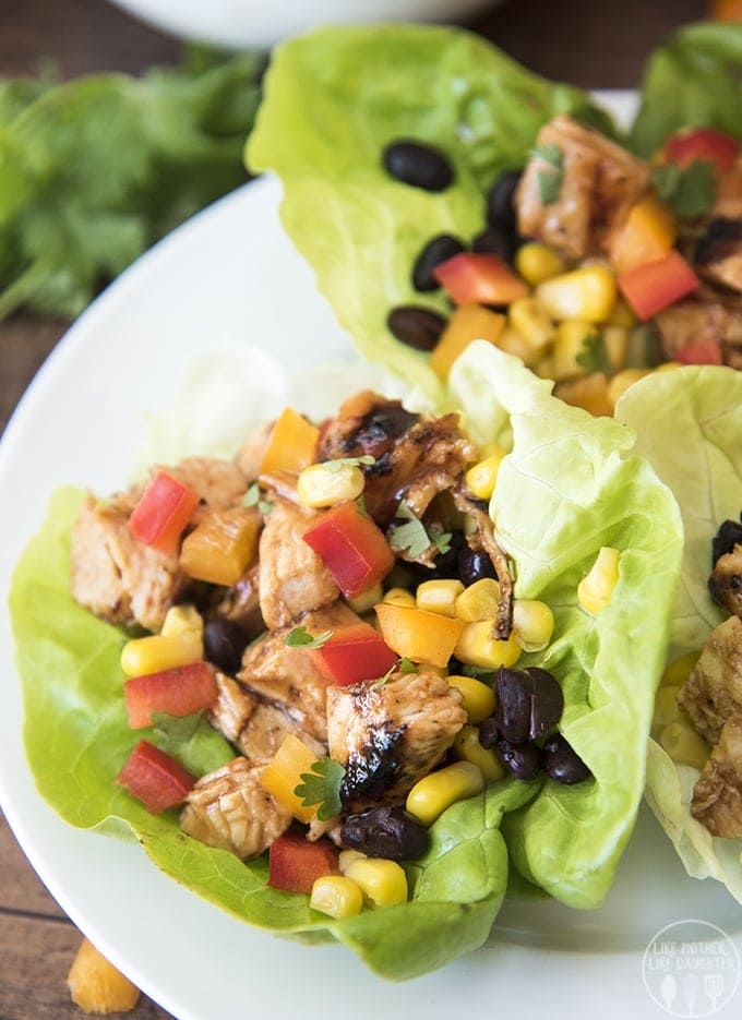 Lettuce wraps topped with bbq grilled chicken, red bell pepper, black beans, and corn on a plate.