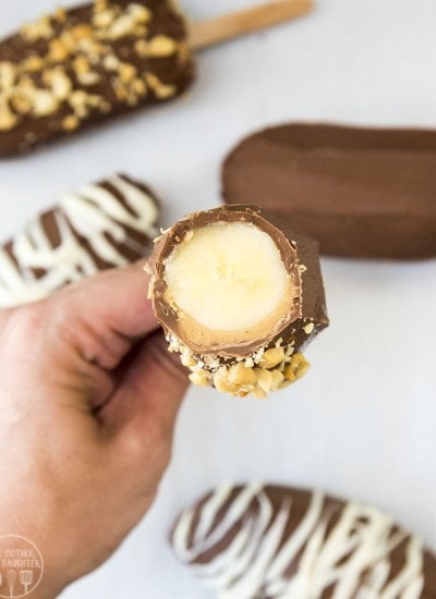 A hand holding a chocolate and peanut butter covered banana with the top cut off showing the banana in the middle.