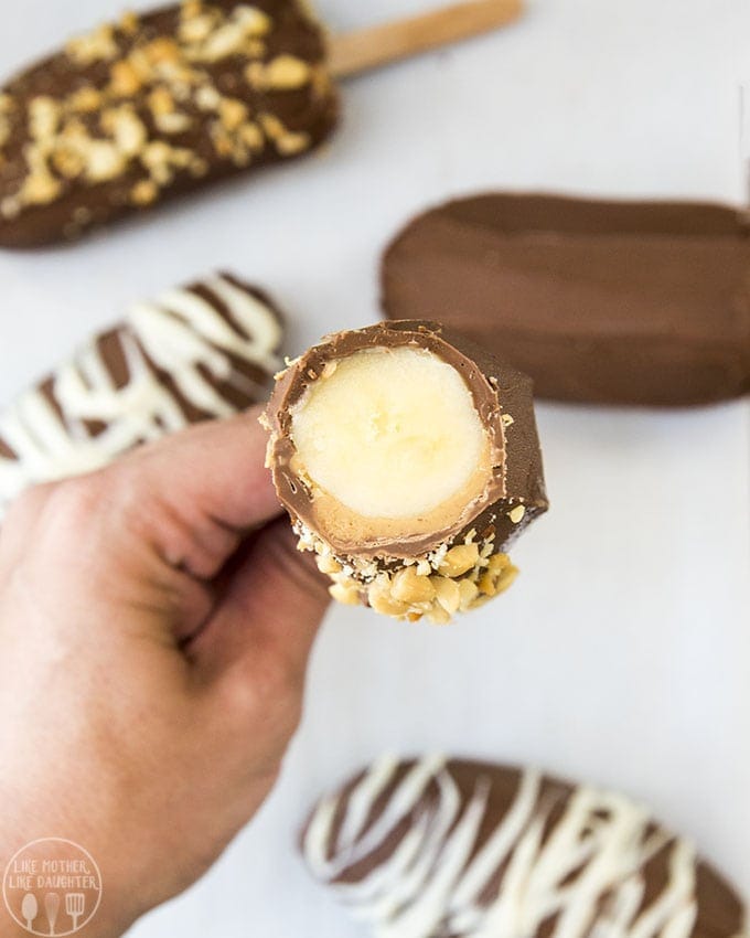 A hand holding a chocolate and peanut butter covered banana with the top cut off showing the banana in the middle.