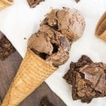 A chocolate ice cream cone with brownie pieces next to it.