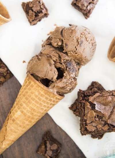 A chocolate ice cream cone with brownie pieces next to it.