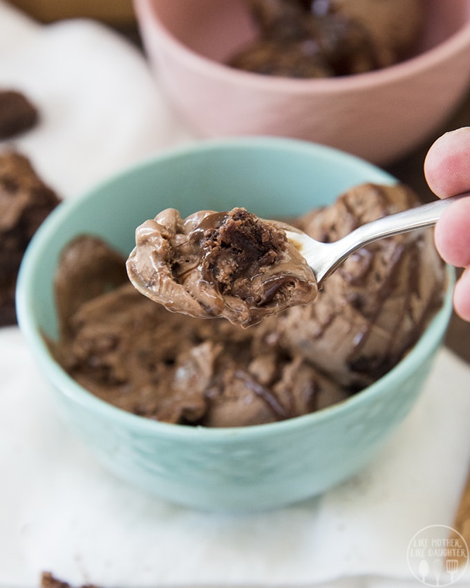 A spoon of chocolate ice cream held above the bowl with a hand.